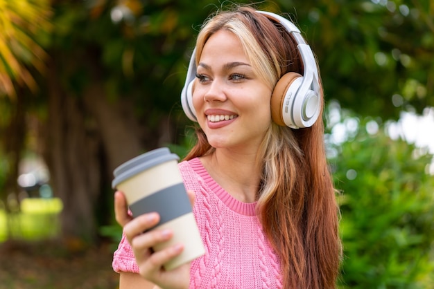 Young pretty woman at outdoors listening music and holding a take away coffee