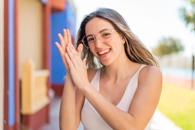 Young pretty woman at outdoors With glasses and applauding