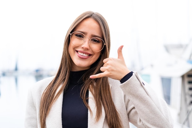 Young pretty woman at outdoors With glasses and doing phone gesture