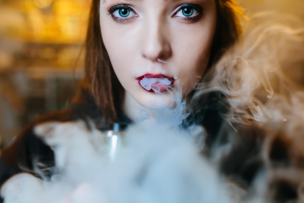 Young pretty woman in red cap smoke an electronic cigarette at the vape shop hiphop style closeup