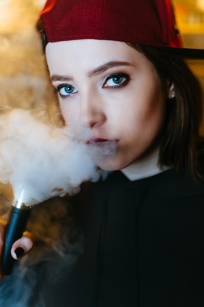 Young pretty woman in red cap smoke an electronic cigarette at the vape shop hiphop style closeup