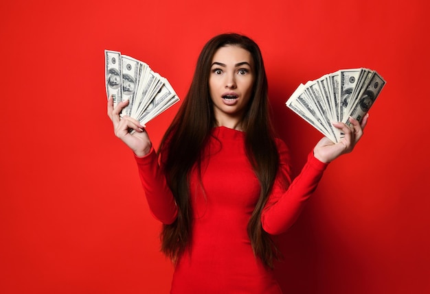 Young pretty woman in red dress hiding behind bunch of money banknotes