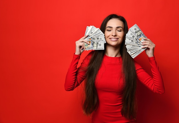 Young pretty woman in red dress hiding behind bunch of money banknotes