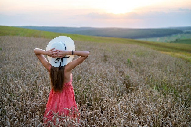 Photo young pretty woman in red summer dress and straw hat standing on yellow farm field