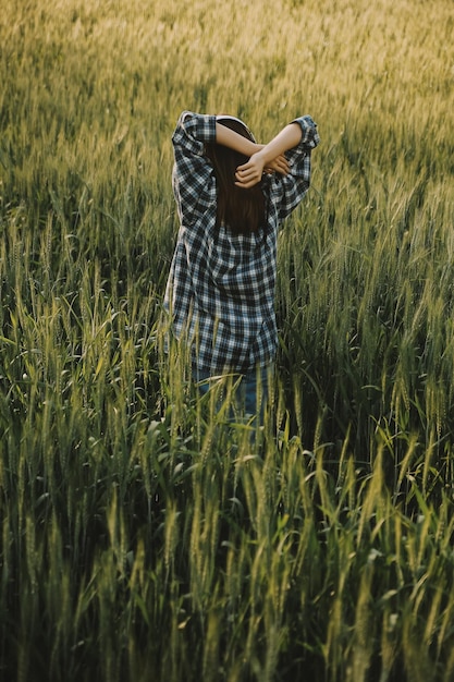 Young pretty woman in red summer dress and straw hat walking on yellow farm field with ripe golden wheat enjoying warm evening