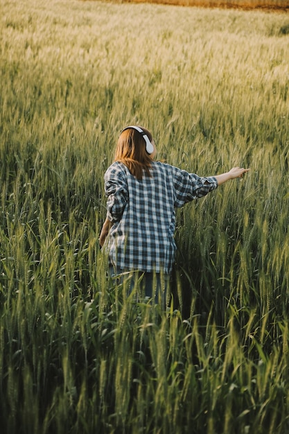 Young pretty woman in red summer dress and straw hat walking on yellow farm field with ripe golden wheat enjoying warm evening