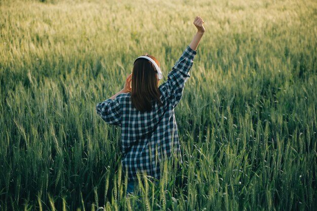 Young pretty woman in red summer dress and straw hat walking on yellow farm field with ripe golden wheat enjoying warm evening