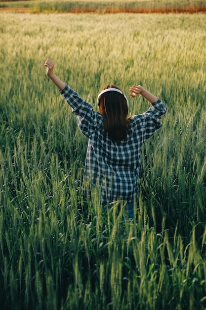 Young pretty woman in red summer dress and straw hat walking on yellow farm field with ripe golden wheat enjoying warm evening