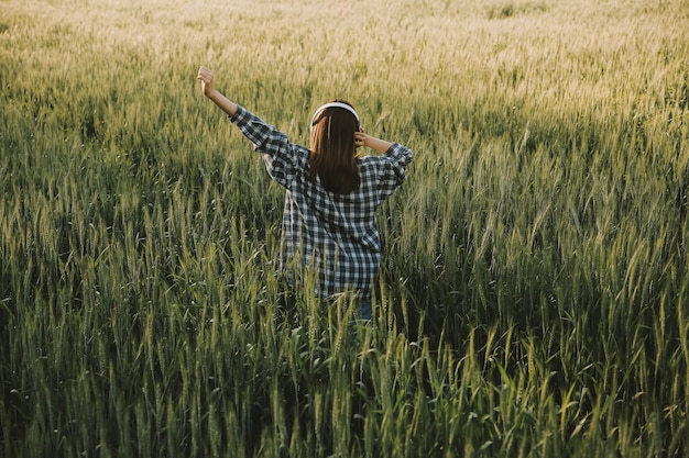 Young pretty woman in red summer dress and straw hat walking on yellow farm field with ripe golden wheat enjoying warm evening