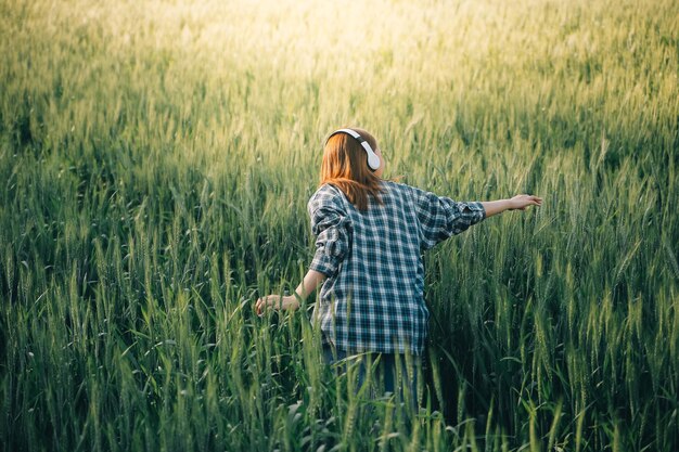 Photo young pretty woman in red summer dress and straw hat walking on yellow farm field with ripe golden wheat enjoying warm evening