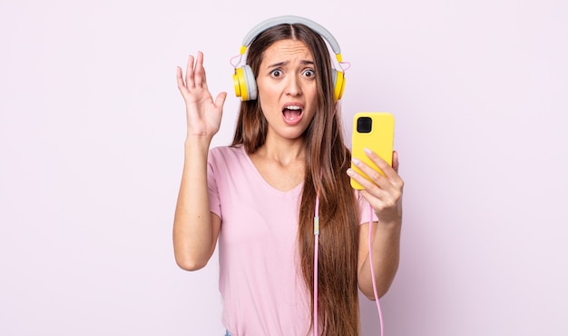 young pretty woman screaming with hands up in the air. headphones and smartphone