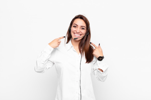 Young pretty woman smiling confidently pointing to own broad smile, positive, relaxed, satisfied attitude with headphones and microphone