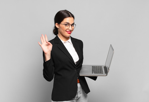 Young pretty woman smiling happily and cheerfully, waving hand, welcoming and greeting you, or saying goodbye. laptop concept