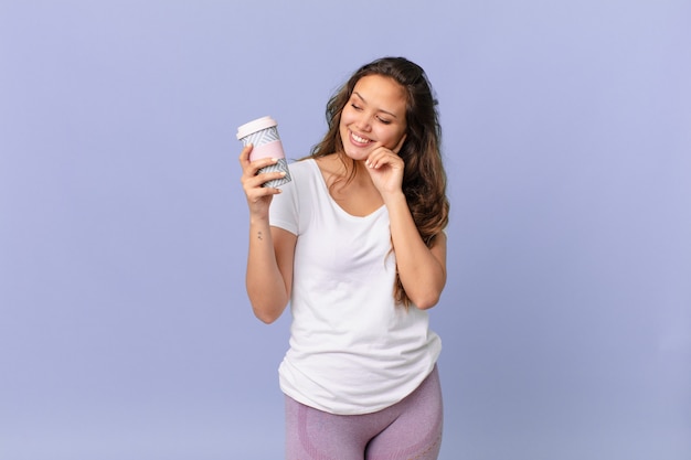 Young pretty woman smiling happily and daydreaming or doubting and holding a coffee