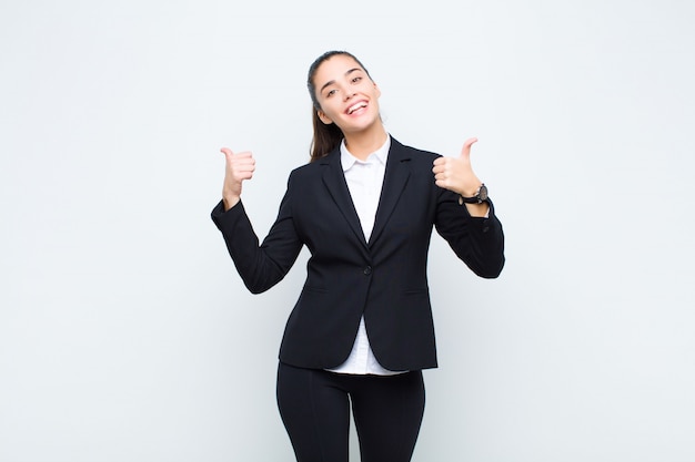 Young pretty woman smiling joyfully and looking happy, feeling carefree and positive with both thumbs up business concept