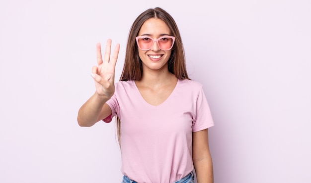 Young pretty woman smiling and looking friendly, showing number three. pink sunglasses concept