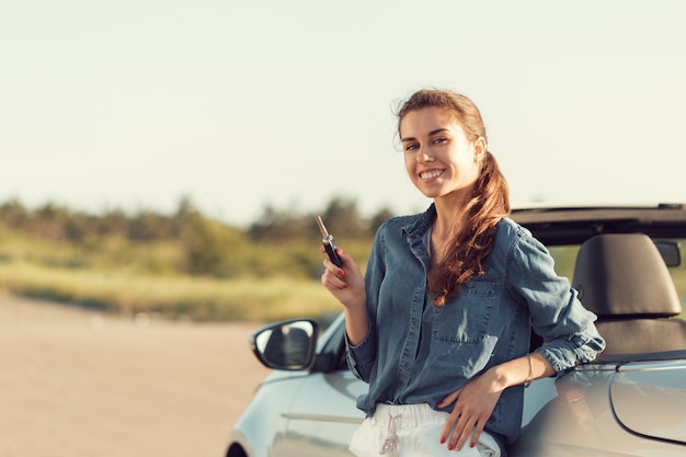 Young pretty woman standing near convertible with keys in hand