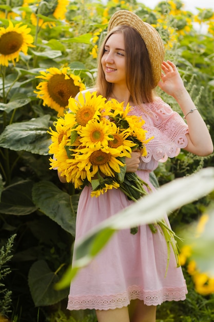 Young pretty woman stands among blooming sunflowers