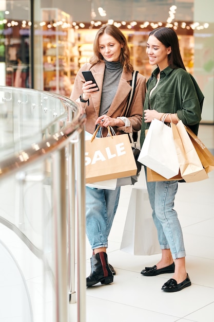 Young pretty woman in stylish casualwear showing her friend new clothing items in online shop while both discussing them in trade canter