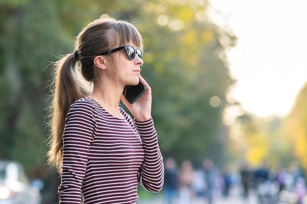 Young pretty woman talking on mobile phone on warm autumn day on a city street outdoors.