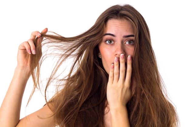 Young pretty woman touching her long brown tangled hair closing mouth by her hand on white background in studio