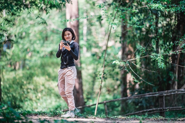 Young pretty woman use digital camera taking a photo beautiful nature while camping in forest with happiness copy space