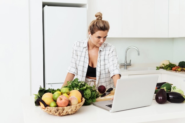 Young pretty woman using laptop for online recipe search to cook at home