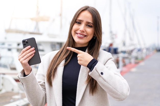 Young pretty woman using mobile phone at outdoors and pointing it