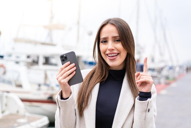 Young pretty woman using mobile phone at outdoors pointing up a great idea