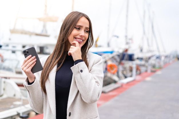 Young pretty woman using mobile phone at outdoors thinking an idea and looking side