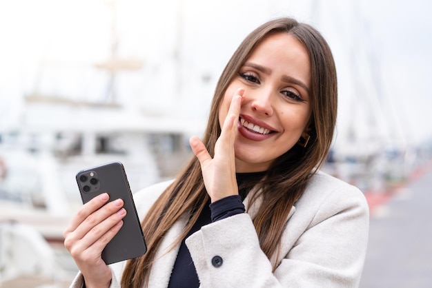 Young pretty woman using mobile phone at outdoors whispering something