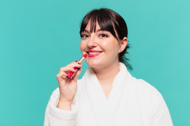 Young pretty woman wearing bathrobe happy expression and holding a lipstick