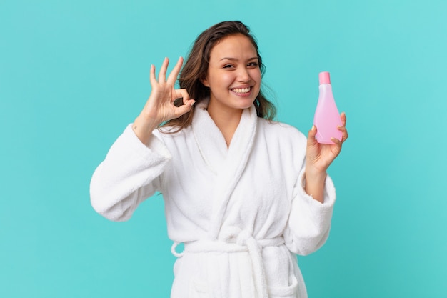 Young pretty woman wearing bathrobe and holding a clean product bottle