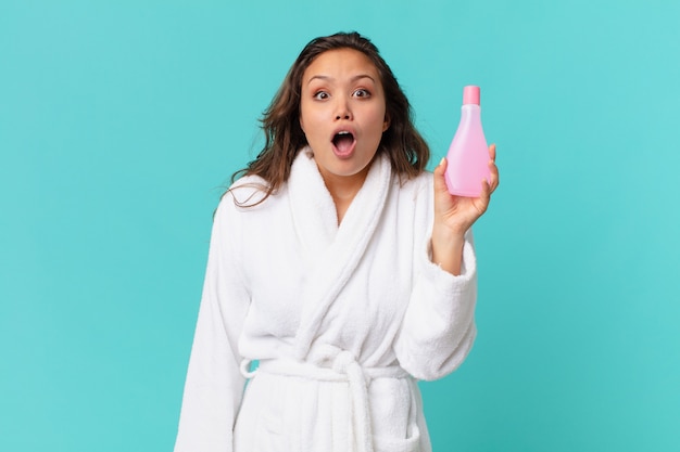 Young pretty woman wearing bathrobe and holding a clean product bottle