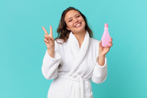 Young pretty woman wearing bathrobe and holding a clean product bottle