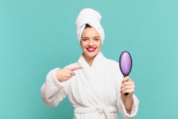 Young pretty woman wearing bathrobe pointing or showing and holding a hairbrush