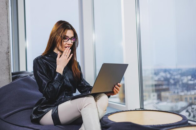 Young pretty woman wearing glasses is working on a laptop while sitting in a modern workspace Remote work freelance