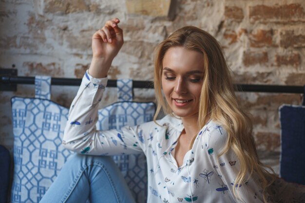 Young pretty woman wearing in white blouse resting on sofa in cafe