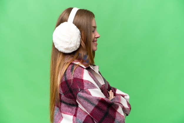 Young pretty woman wearing winter muffs over isolated chroma key background in lateral position