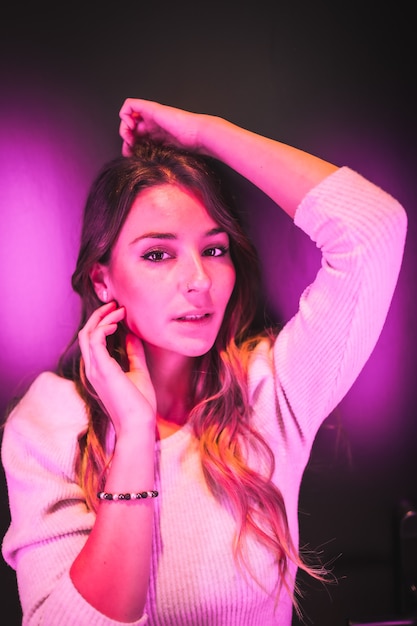 Young pretty woman in white sweater looking at camera with sweet eyes with pink and blue led lights