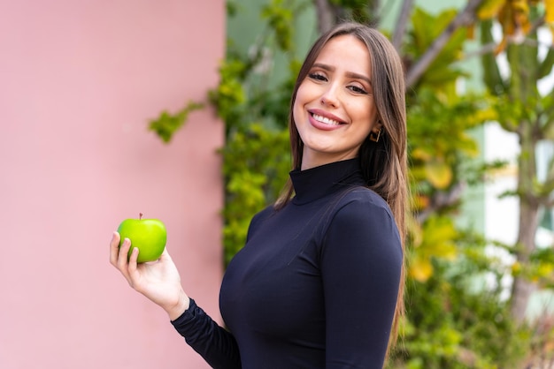 Young pretty woman with an apple at outdoors smiling a lot