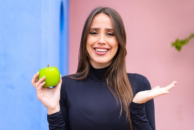 Young pretty woman with an apple at outdoors with shocked facial expression