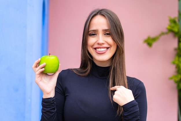 Young pretty woman with an apple at outdoors with surprise facial expression