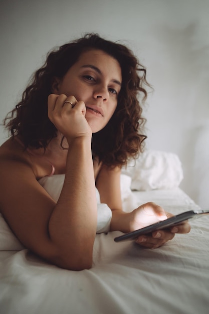 Young pretty woman with curly hair in bed with phone