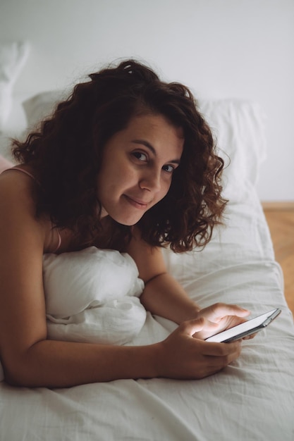 Young pretty woman with curly hair in bed with phone