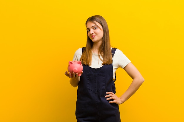 Young pretty woman with a piggy bank  against orange 