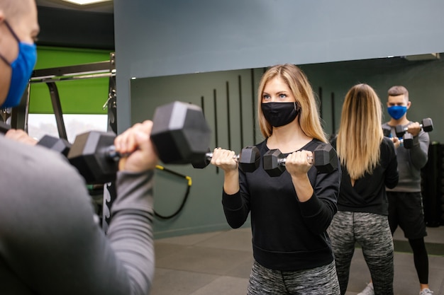 Young pretty woman with protective mask working out with personal trainer at the gym during Covid-19 pandemic