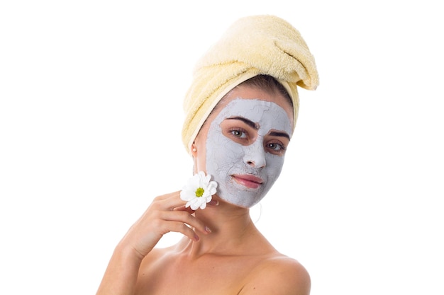 Young pretty woman with yellow towel on her head and cosmetic mask on her face holding white flower