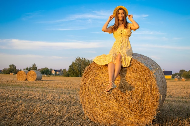 Young pretty woman in yellow dress and hat close up on the field background with haystacks at sunset time