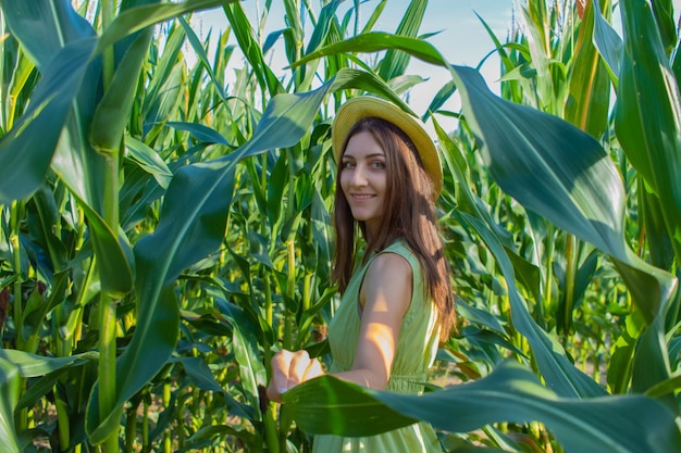 Young pretty woman in the yellow hat among the corn plants in the corn field in summer season Bereza Belarus